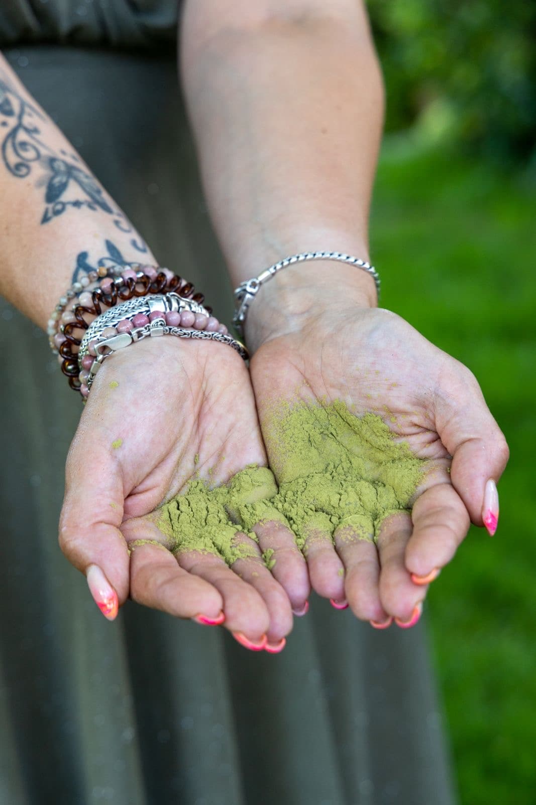Handen met een houten kom natuurlijke groene plantenkleurpoeder en kwast